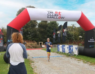 Red and white inflatable arch with full-colour branding at a sports event, used for race start/finish line signage.